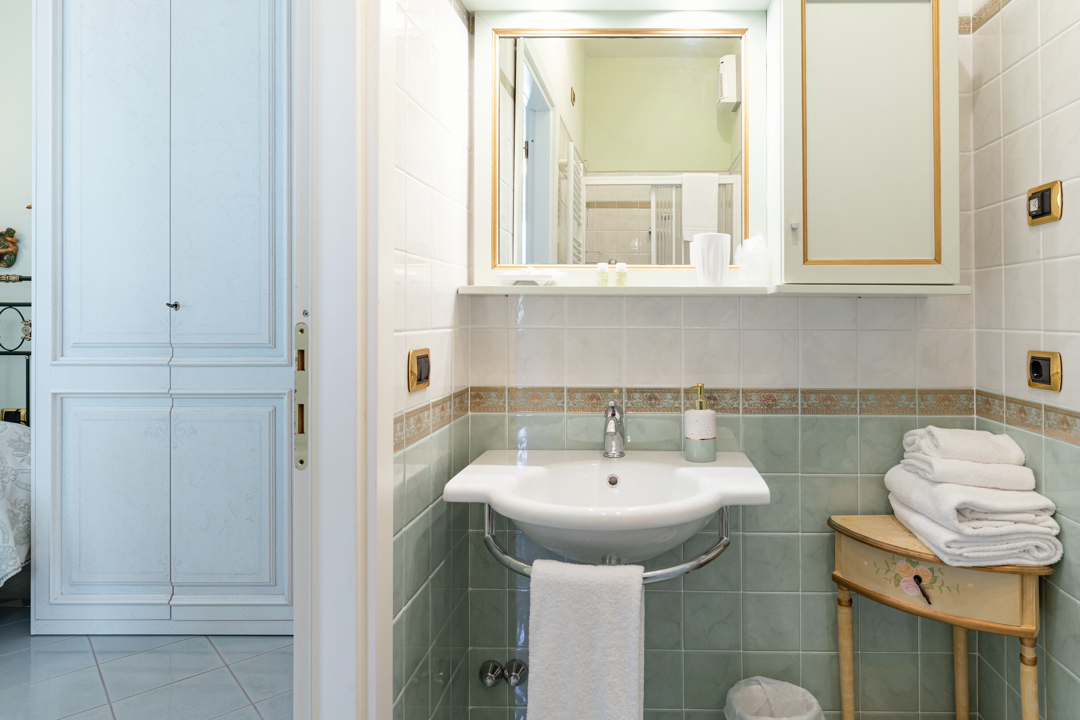A bathroom with a white sink, a mirror, and a small wooden vanity with towels.