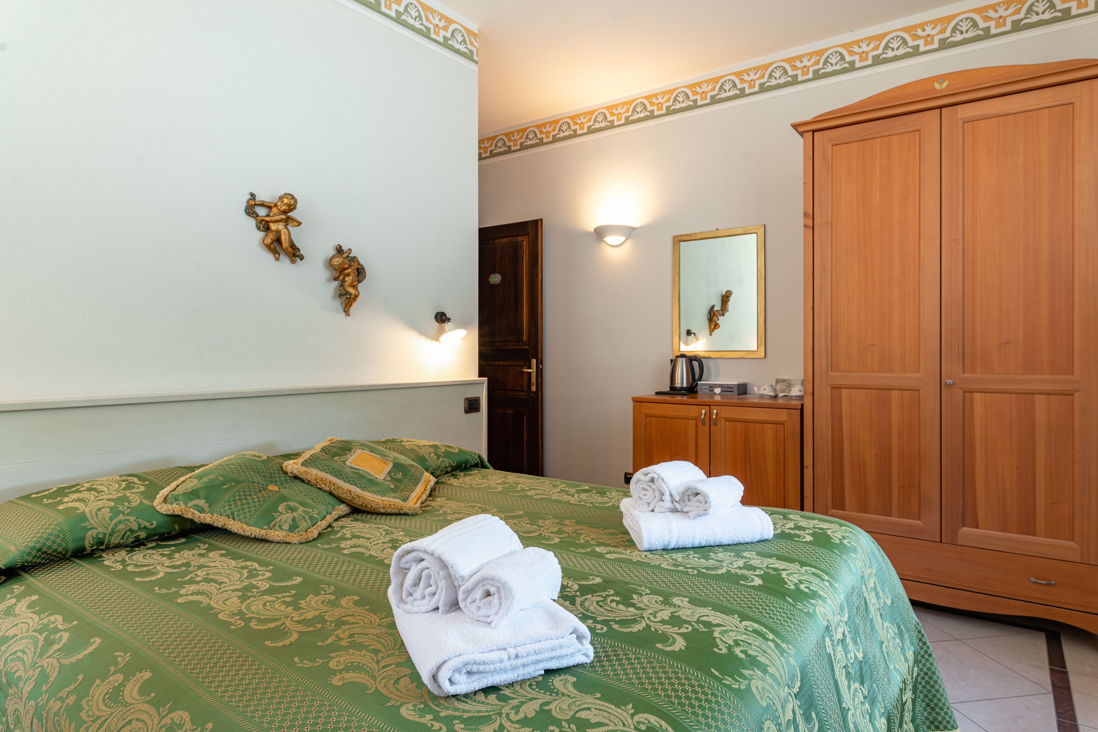 Une chambre d’hôtel avec une couvre-lit à motifs verts, une armoire en bois et un miroir fixé au mur.