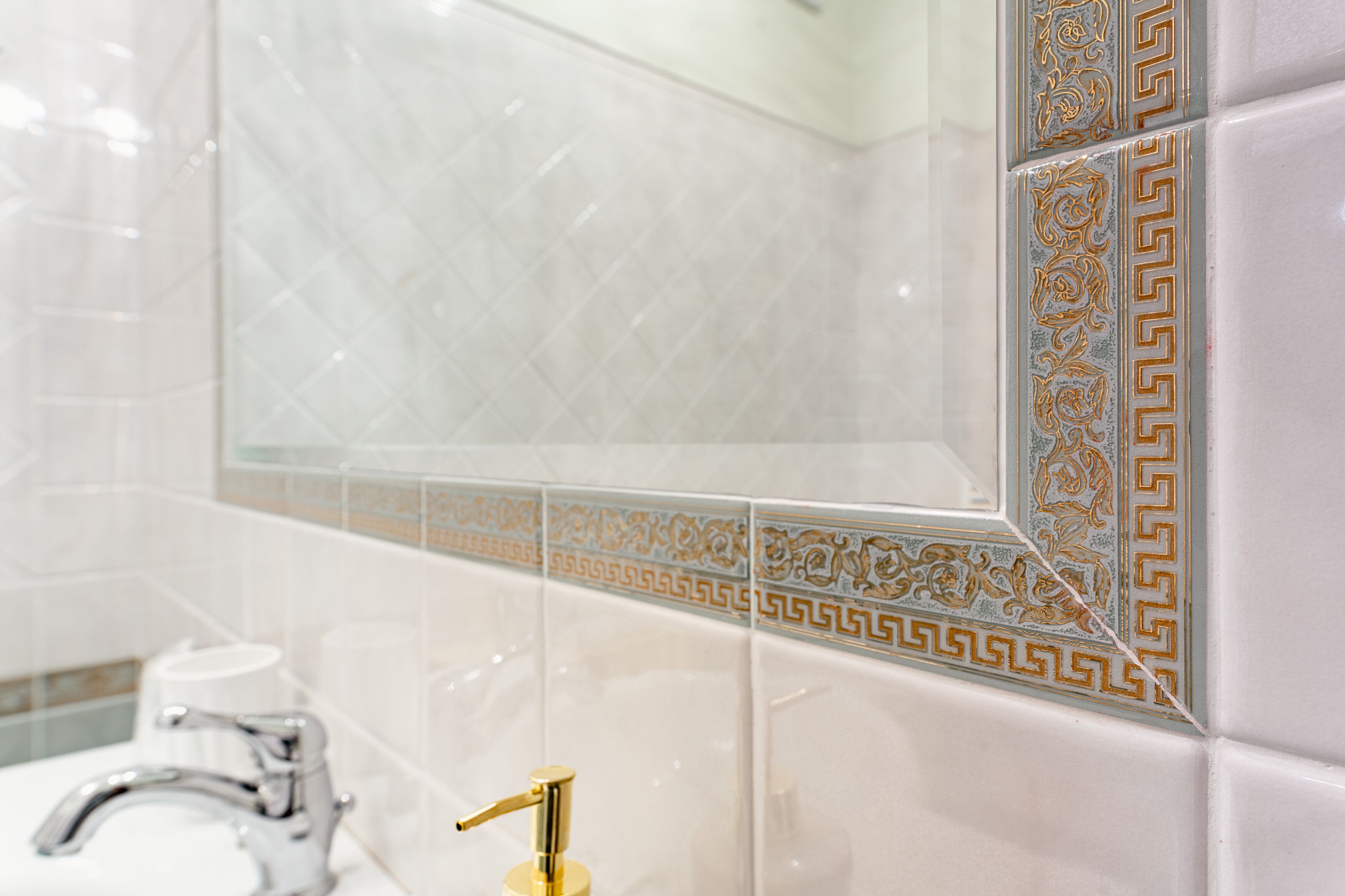 A bathroom with white tiles, a gold faucet, and decorative tiles with a geometric pattern.