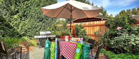 An outdoor patio with a table set for dining, a grill, and a covered umbrella.