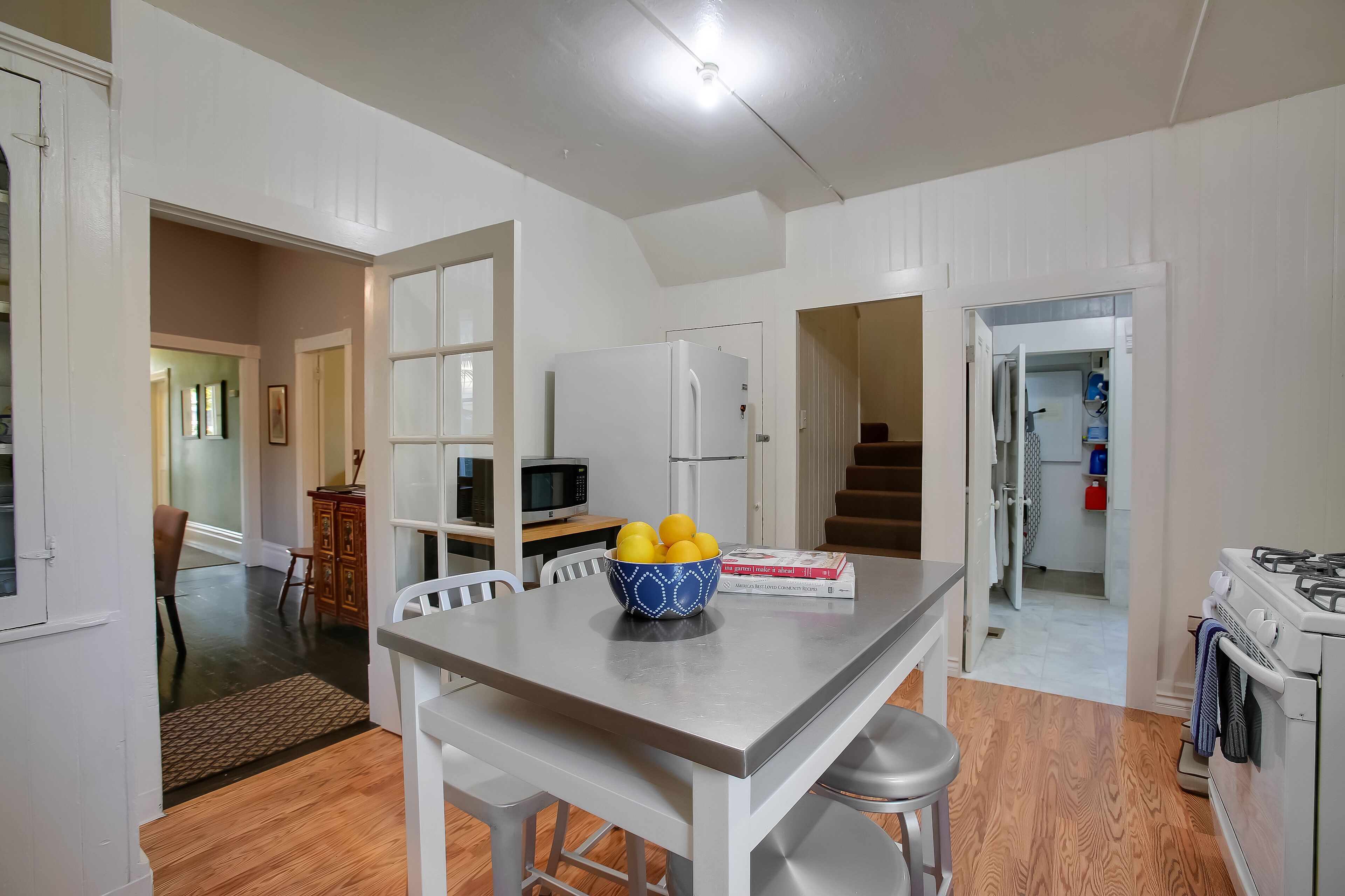 A kitchen with a white refrigerator, a microwave, and a stove. There is a dining table with a bowl of lemons and a book.