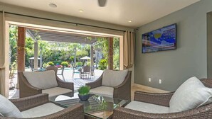 A modern living room with wicker furniture, a glass coffee table, and a view of an outdoor pool area. - Endless Escape Urban Apartment | Galleria Escape (Houston)