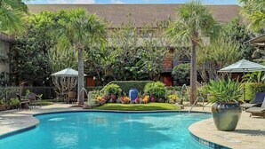 A swimming pool with a tiled edge, surrounded by lush greenery and palm trees. - Endless Escape Urban Apartment | Galleria Escape (Houston)