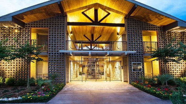 A modern building with a wooden facade, a central entrance with a metal gate, and a balcony on the upper floor. - Endless Escape Urban Apartment | Galleria Escape (Houston)