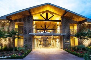 Un bâtiment moderne doté d’une façade en bois, d’une entrée centrale avec un portail en métal et d’un balcon à l’étage supérieur.