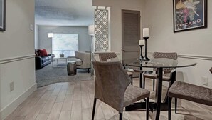 A dining area with a round table and four chairs, a sofa, a coffee table, and a decorative screen. - Endless Escape Urban Apartment | Galleria Escape (Houston)