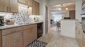 A modern kitchen with wooden cabinets, a tiled backsplash, and a central island. - Endless Escape Urban Apartment | Galleria Escape (Houston)