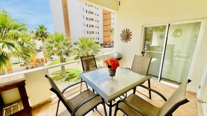 Ein Balkon mit Glastisch, zwei Stühlen und einer Blumenvase.
