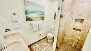 Ein Badezimmer mit Badewanne, Toilette und Duschbereich. An der Wand hängt ein Bild und eine Handtuchstange mit Handtüchern.