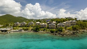 A coastal resort with multiple buildings featuring large windows and balconies, situated near turquoise waters and a mountainous backdrop.