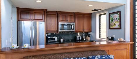 A kitchen with wooden cabinets, stainless steel appliances, a black countertop, and a wicker bench with patterned cushions.