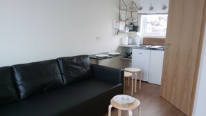 A compact living space with a black sofa, a small dining table with plates, and a kitchen area with a sink and cabinets. - Vatnsás 10 (Stykkisholmur)