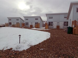 Une rangée de bâtiments blancs avec des portes numérotées, un chemin de gravier et une clôture en bois.