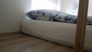 A bedroom with a bed, a window with a blind, and a wooden floor. - Vatnsás 10 (Stykkisholmur)