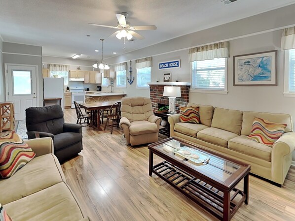 A spacious living room with a sofa, armchairs, and a coffee table. A kitchen area with a dining table and chairs is visible in the background.