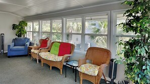 A sunlit room with wicker furniture, large windows, and a potted plant.