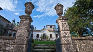 Un portón de piedra con dos pilares ornamentales que conduce a un edificio de fachada blanca y césped verde.