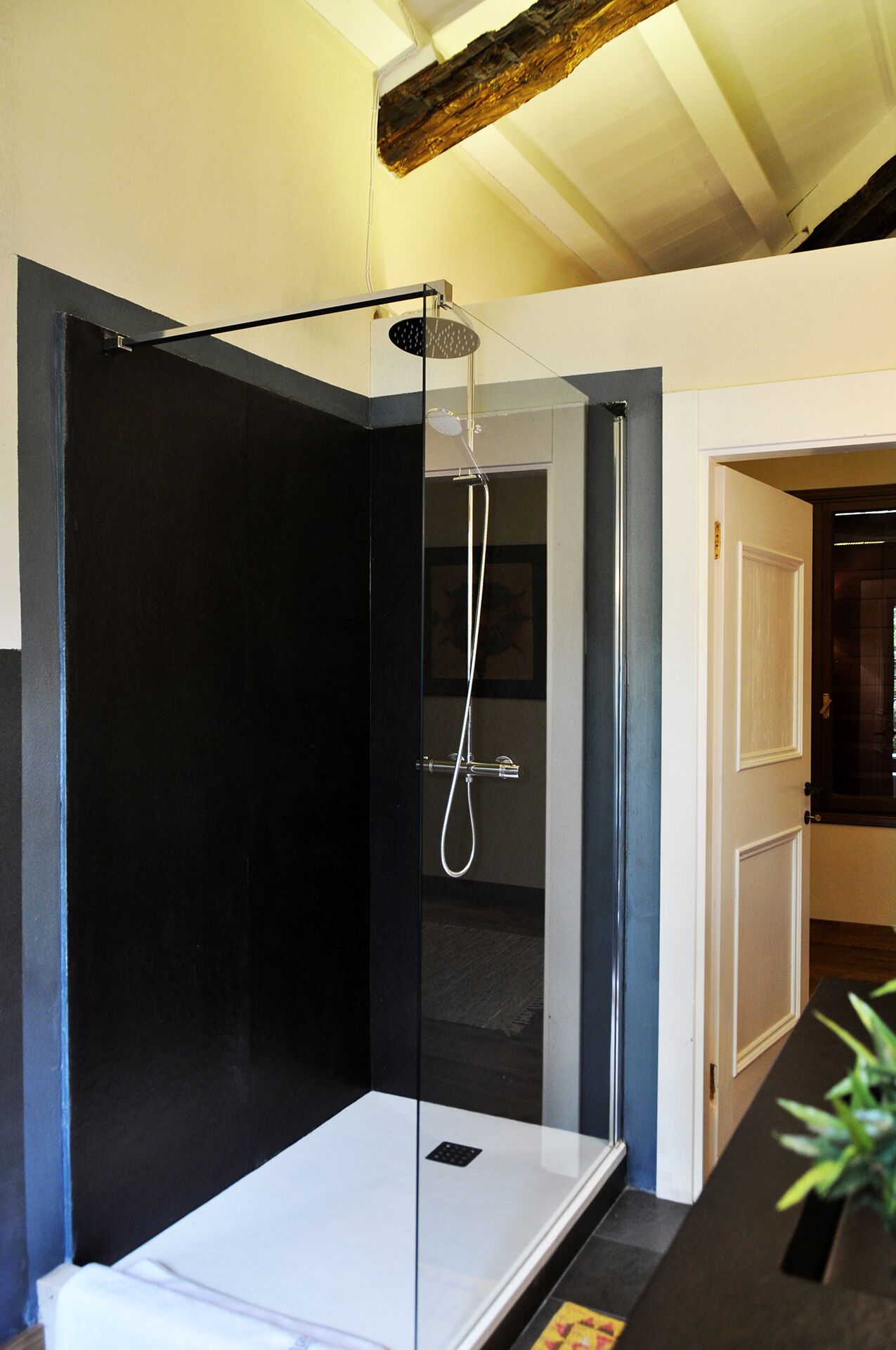 Une salle de bain moderne avec une douche à parois de verre, une baignoire blanche et une poutre en bois au plafond.