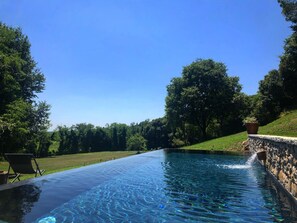 A clear blue infinity pool with a stone wall on one side and a grassy area with trees on the other.