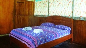 Uma cama de solteiro com colcha estampada, cabeceira de madeira e cortinas com padrão floral.