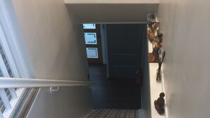 Gradi amb catifes i barana, una prestatgeria penjada a la paret amb objectes decoratius, i una porta que dona a un altre espai.