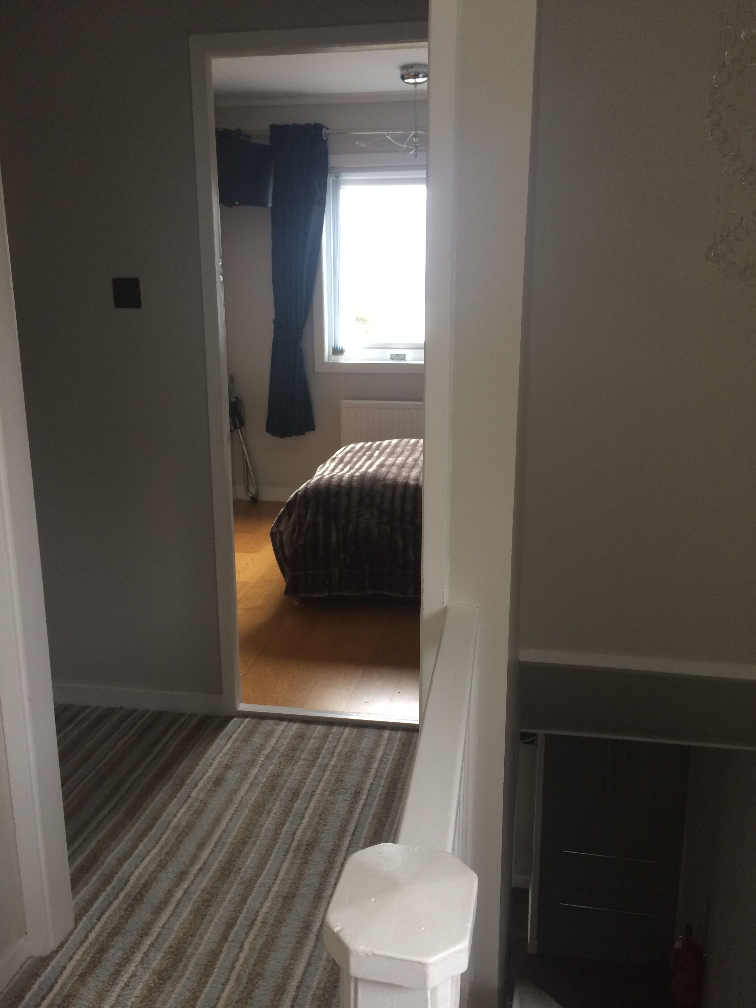 A bedroom with a bed, a window with curtains, a radiator, and a white chair.