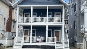A two-story house with a front porch, a chimney, and a sign indicating it is for sale.