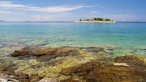 A clear view of a rocky shoreline with shallow water leading to a small island with trees. - Apartment in Murter with Terrace, Air condition, WIFI, Washing machine (125-3) (Murter)