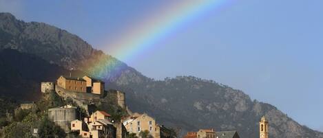 A town with historic buildings and a castle on a hill, with a rainbow in the sky.