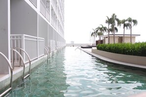 A swimming pool with clear water, surrounded by a white building with balconies and palm trees. - Penthouse Floor Overlooking Manila Bay (Pasay)