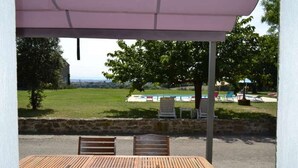 Un espace extérieur abrité, aménagé avec des sièges, et offrant une vue sur une piscine et un paysage verdoyant.