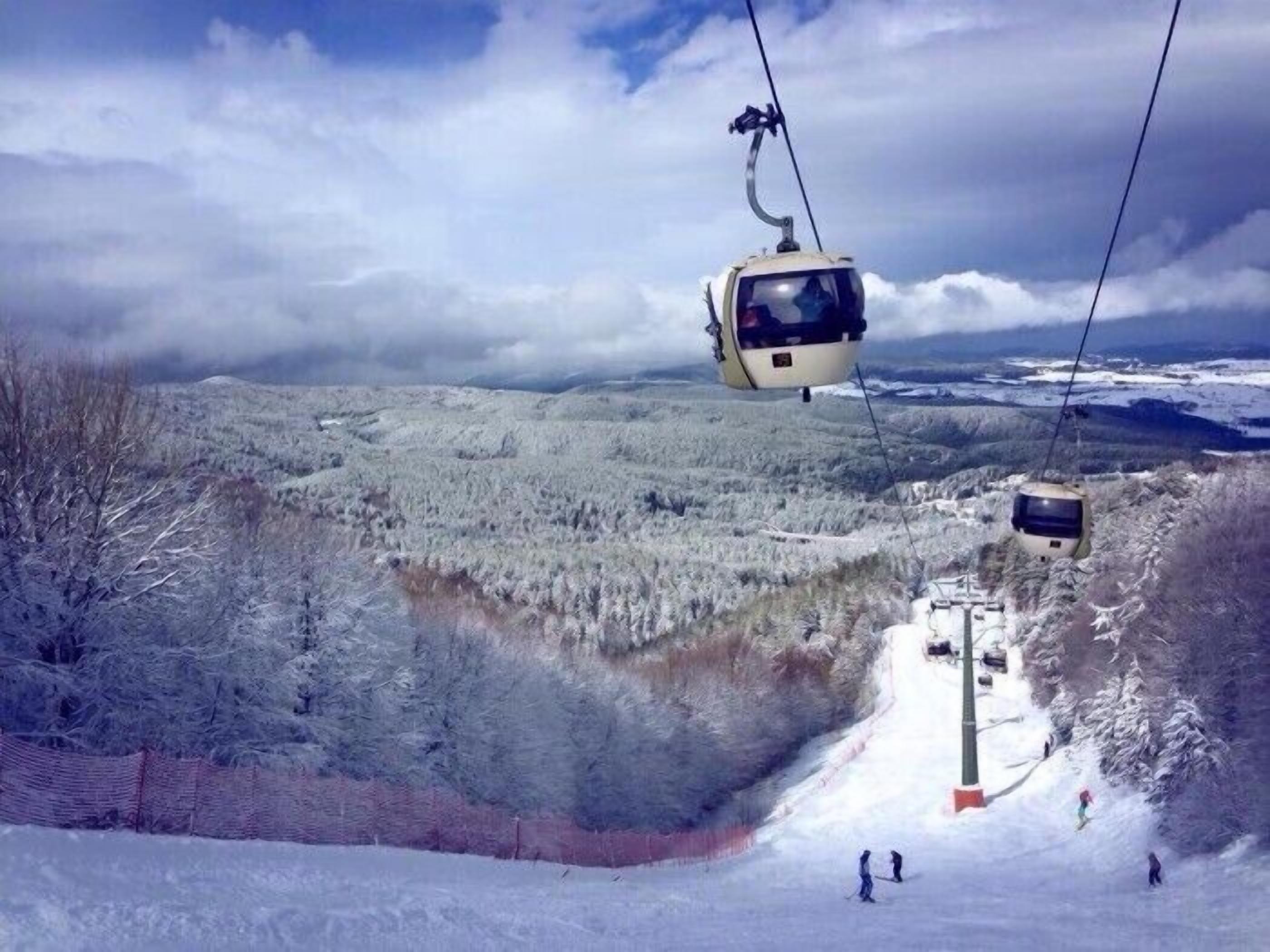 A cable car system in a mountainous area with snow-covered terrain and a clear sky.