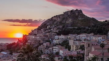 A coastal town at sunset with a prominent hill and a church on top.