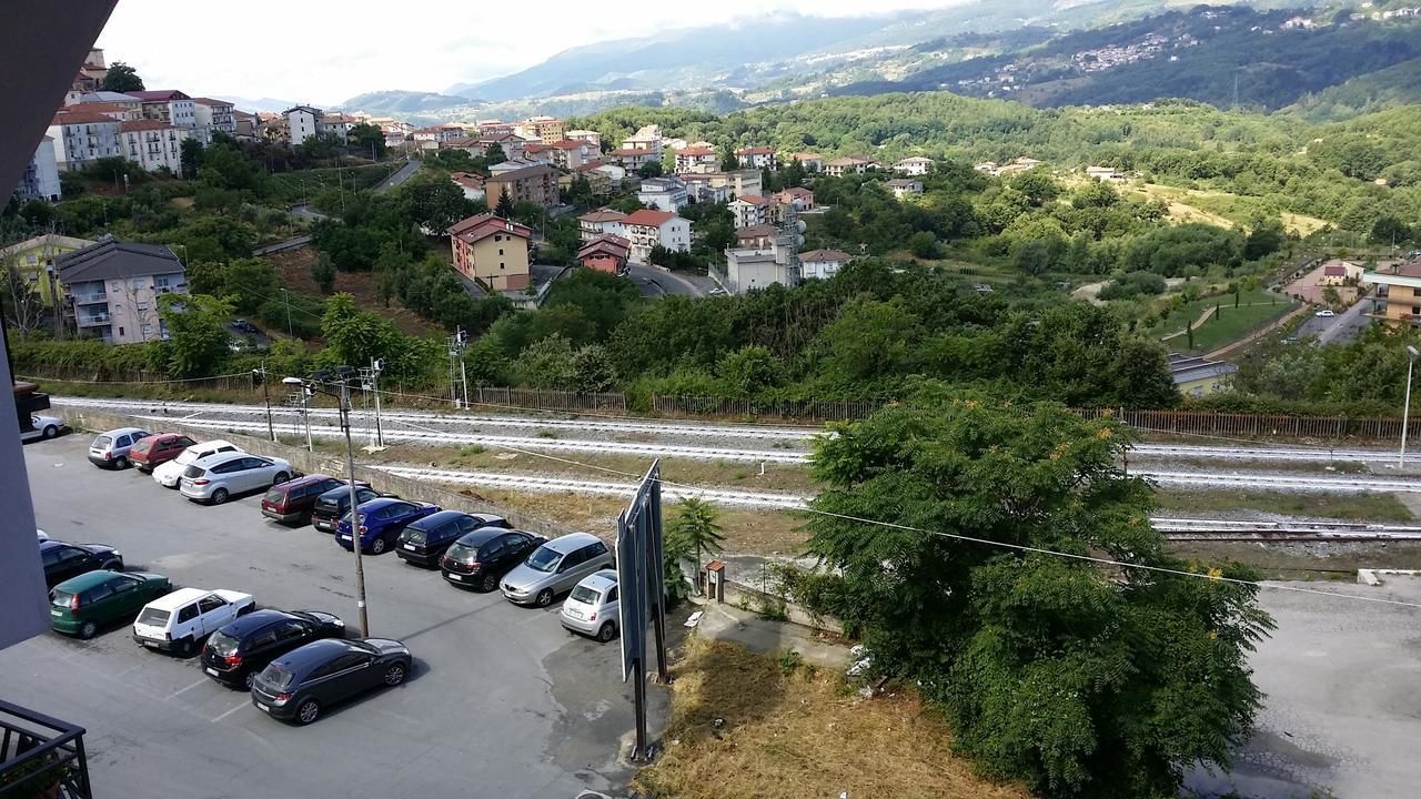 Un aparcamiento con varios coches, una vía de tren y una zona residencial al fondo.