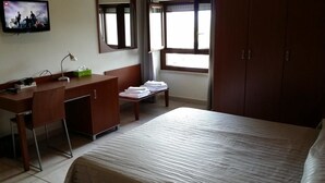 A hotel room with a bed, a desk with a lamp, a TV, and a window with curtains. - Il Tulipano (Rogliano)