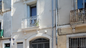 Un edificio de varios pisos con balcones, una entrada amplia en arco y ventanas protegidas con barrotes.