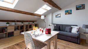 Una sala de estar acogedora con techo de madera, un sofá, una mesa de comedor con una silla y una pequeña mesita auxiliar.