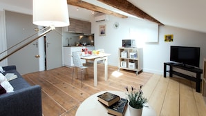 Una sala moderna con un sofá, una mesa de comedor y un televisor. Se ve una cocina al fondo con estufa y armarios.