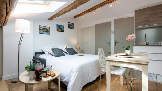 Un dormitorio moderno con tragaluces, una cama con almohadas, una mesita de noche con objetos, una silla y una pequeña mesa.