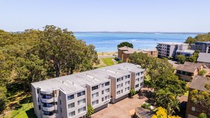 A multi-story building with a flat roof, surrounded by trees and a view of the sea. - Mistral Court 2, 17 Mistral Close - little beach water views & Wifi (Nelson Bay)