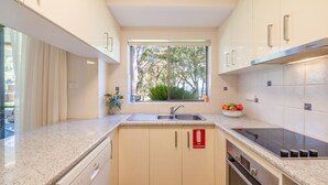 A modern kitchen with a built-in stove, a sink, and a window overlooking a garden. - Mistral Court 2, 17 Mistral Close - little beach water views & Wifi (Nelson Bay)