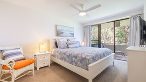 A bedroom with a bed, nightstands, a chair, a desk, a ceiling fan, and a window with curtains.