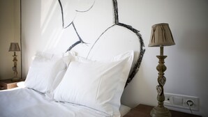 Een keurig opgemaakt bed met witte lakens, een muur met een zwart abstract ontwerp en een klassieke lamp op een nachtkastje.