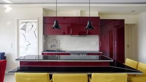 Een moderne keuken met rode kastjes, een zwart aanrecht en gele stoelen.