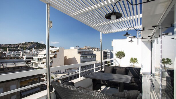 Een balkon met rieten meubilair, een pergola en uitzicht op de stad.