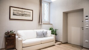 A modern living room with a white sofa, a framed picture on the wall, a window with curtains, and a door with a light switch. - Apartment Verona Historical Center 50 meters from the Arena and Piazza Brà - Opera (Verona)