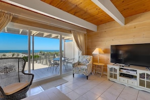 Quarto com televisão, cadeira, mesa e vista para a praia.