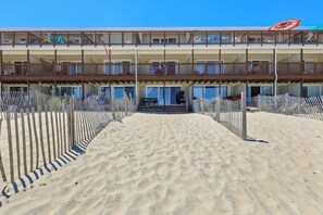 Een hotel aan het strand, bestaande uit een gebouw van twee verdiepingen, met een zandstrand ervoor en een houten omheining.