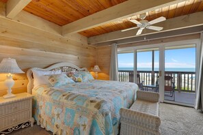 Een slaapkamer met een bed, nachtkastjes, een plafondventilator en uitzicht op het strand door een schuifdeur.