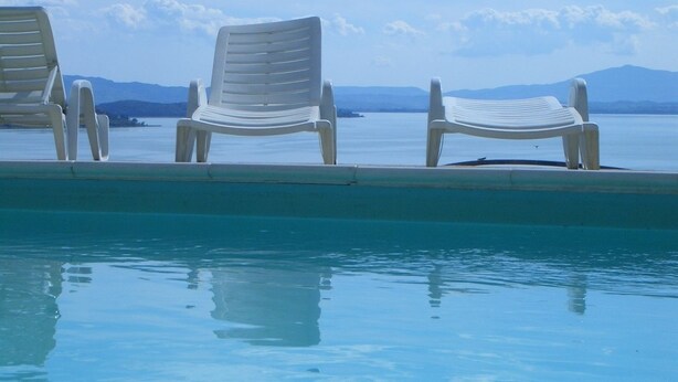 Ein Poolbereich mit drei weißen Plastikstühlen und freiem Blick auf das Meer und ferne Berge.